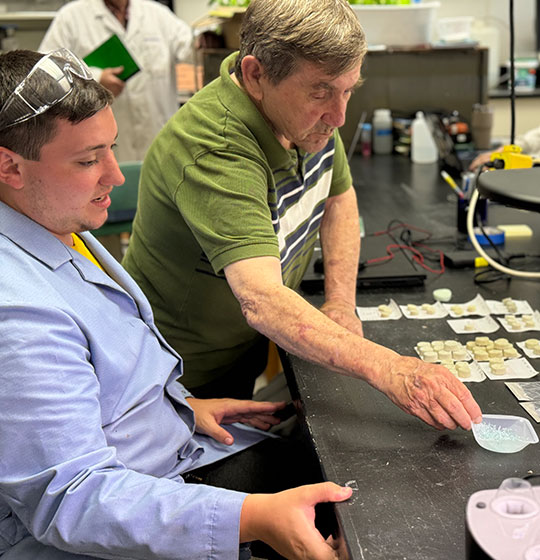 man with lab coat and another man with polo shirt, looking over materials