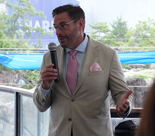 man with beard in suit, wearing glasses, talking with microphone