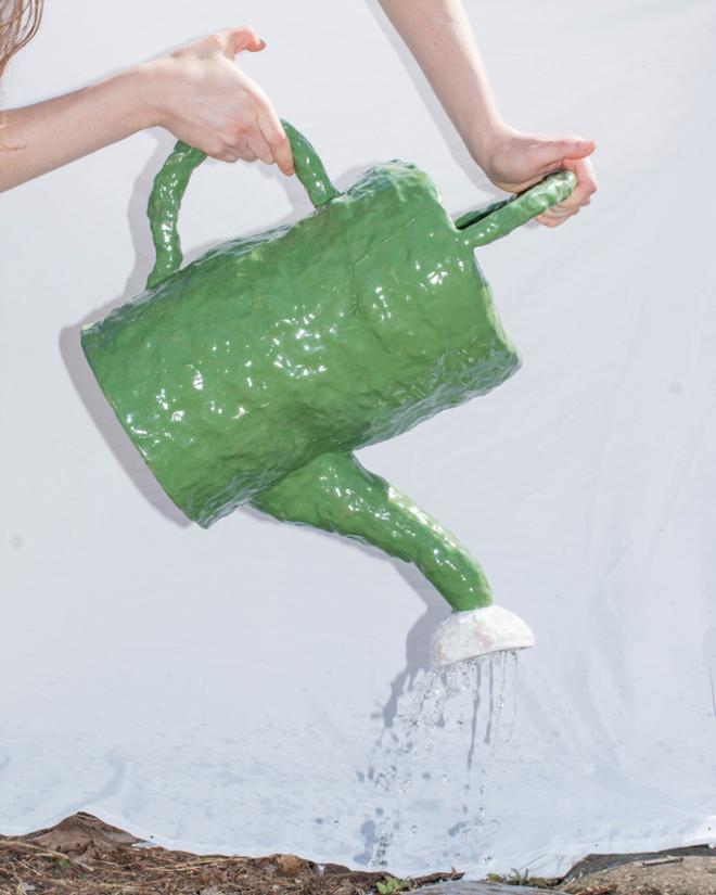 Hands pouring green ceramic watering can.
