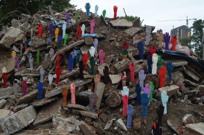 Colorful hands and forearms standing hand-up in a large pile of rubble.