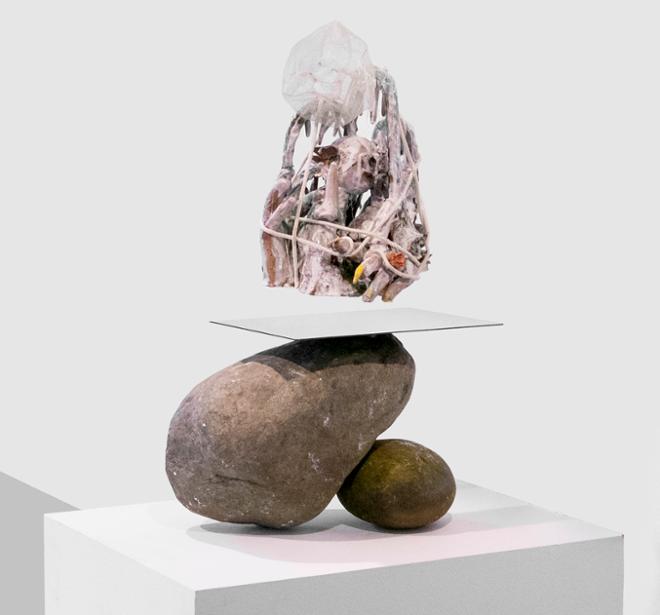 An abstract sculpture balanced on top of two rocks and a mirror.