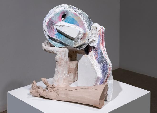A mixed media sculpture resembling the upper body of an abstracted person leaning on their hand.  