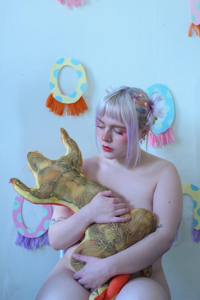 An image of a partially nude person holding an animal-like stuffed object. 