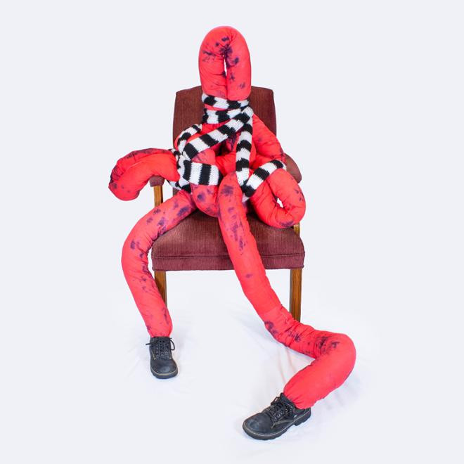 A red, abstracted figure sitting on a chair with a stripped scarf. 