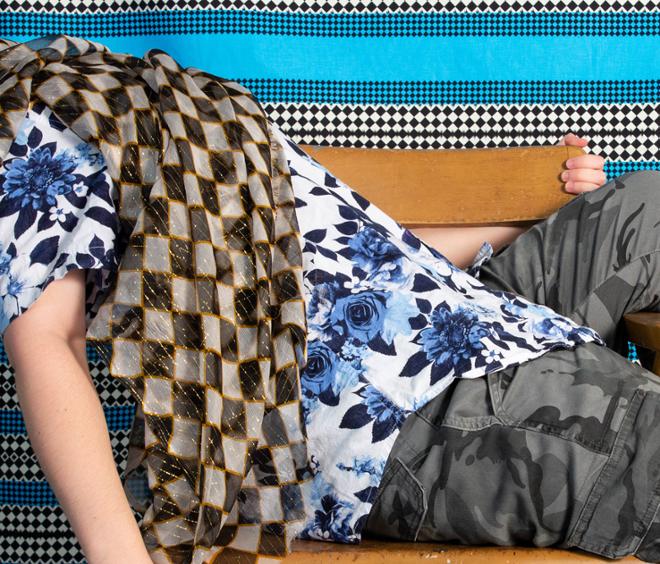 An image of a person covered with fabric on a chair in front of a blue pattern. 