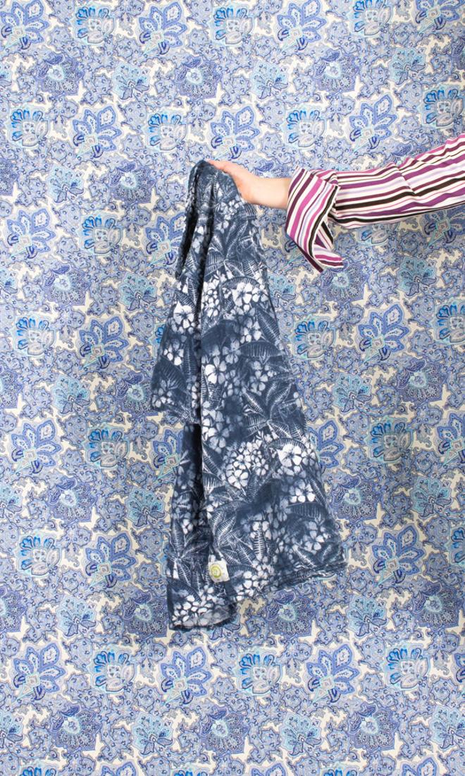 A photograph of an arm holding out a blue patterned fabric in front of a blue pattern.