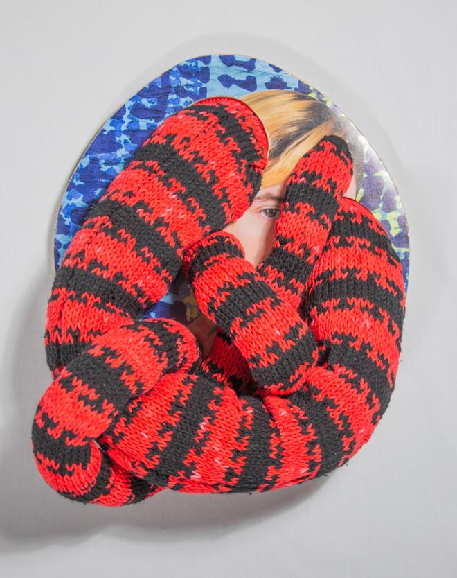 A red and black knitted shape curled on top of a photograph of a face. 
