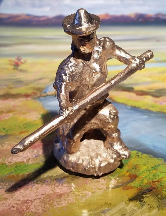 A photograph of a bronze figure kneeling while holding a staff. 