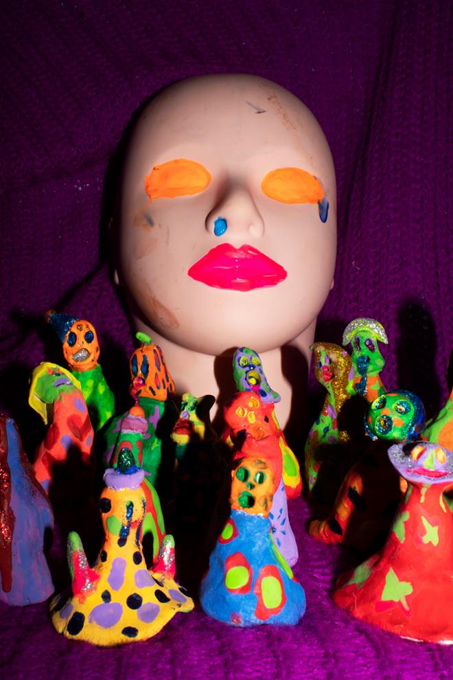 Small, colorful dolls in front of a mask of a face. 