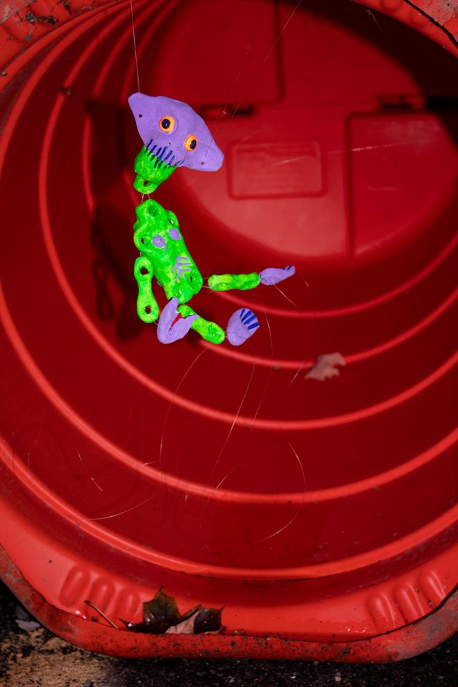 A green and purple doll suspended by string in a red tube. 