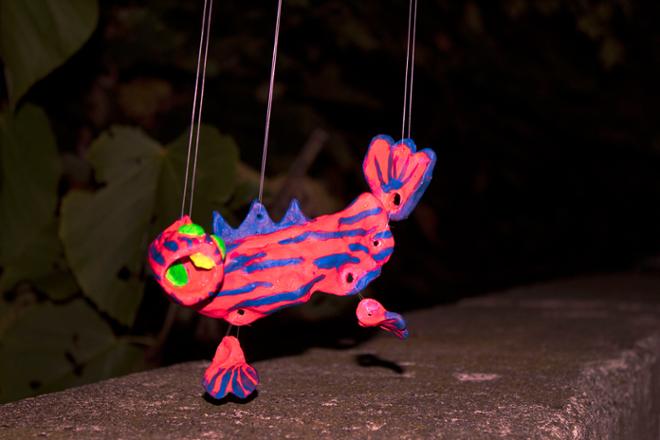 A pink ceramic creature suspended by string outside. 