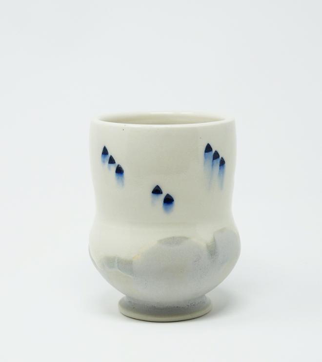  A white ceramic cup with blue dots and a gray bottom. 