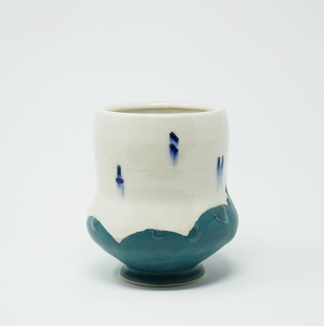 A white ceramic cup with blue dots and a teal bottom. 
